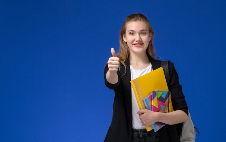 front-view-female-student-black-jacket-wearing-backpack-holding-files-with-copybooks-smiling-blue-wall-college-university-lesson